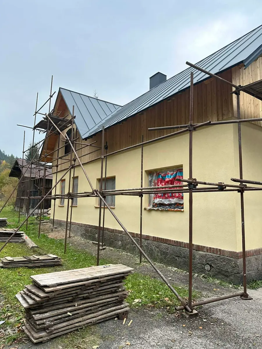 Zateplená fasáda domu na lešení, žlutá omítka a dřevěný obklad štítu, rozpracovaná zakázka